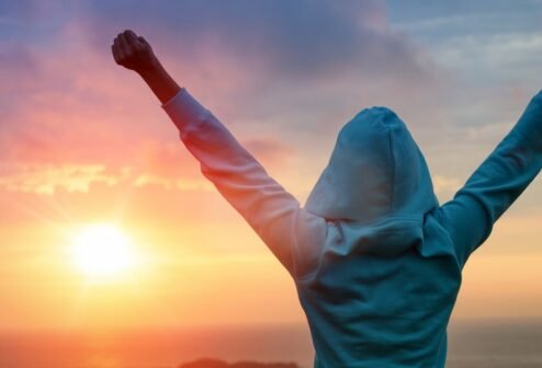 Sport success on sunset background Sport and life achievements and success concept. Rear view sporty girl raising arms towards beautiful glowing sunshine.